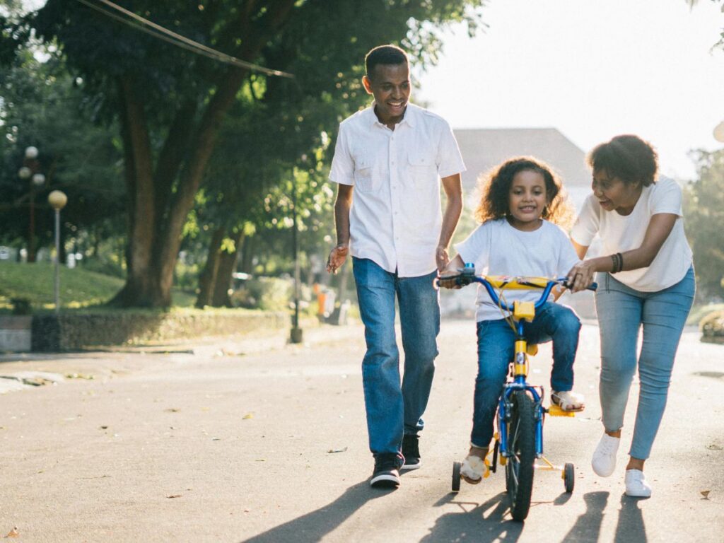 parents teaching their daughter how to ride a bike in park